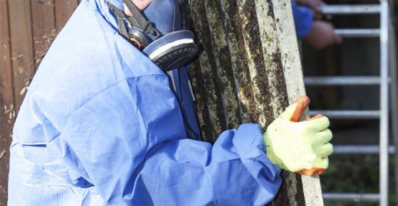 asbestos removal contractor in personal protective equipment removing house siding covered in asbestos