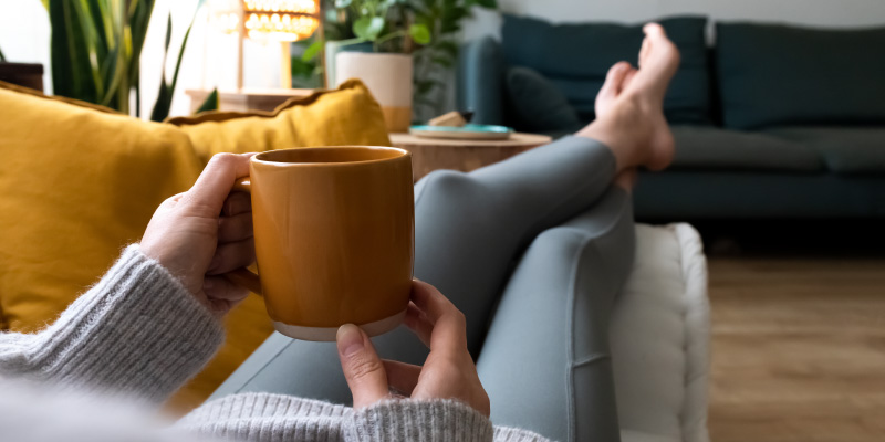 person drinking coffee with feet up on couch